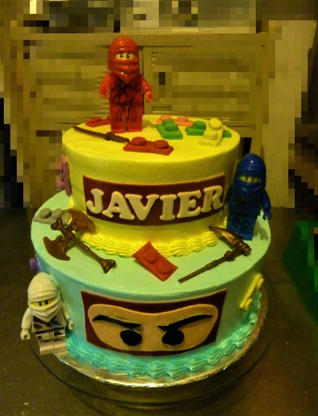 Two-tier Ninjago themed birthday cake with yellow and light blue icing, featuring Lego ninja figures and building block decorations.
