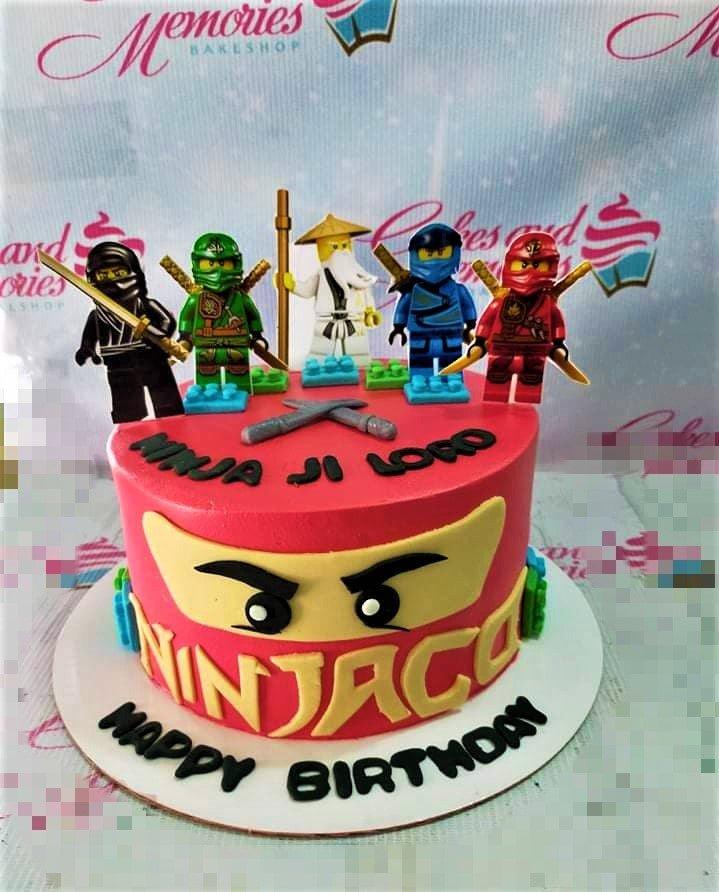 Red Ninjago themed birthday cake with Lego ninja figurines and a large yellow ninja mask design on the side.