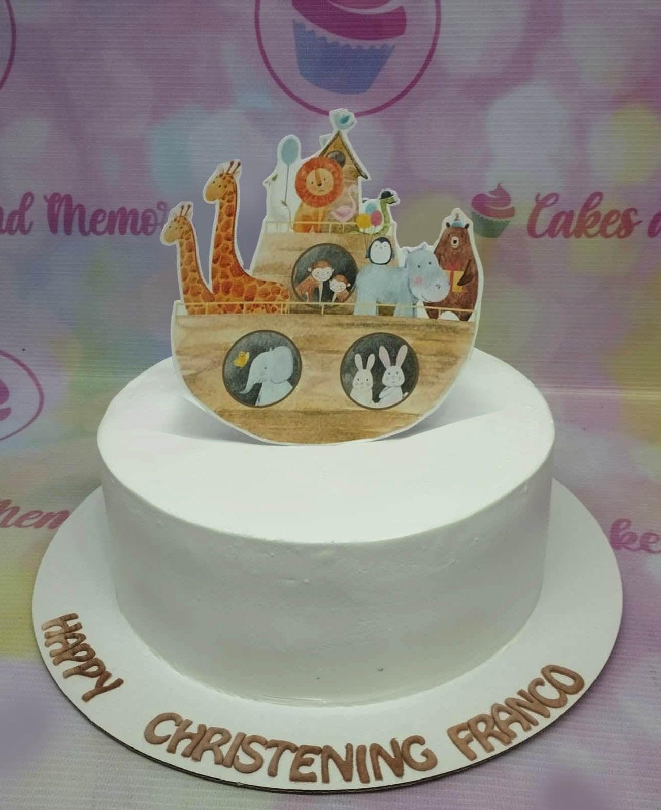 White minimalist christening cake with a large Noah's Ark animal printout topper and brown gumpaste letters on the base board.
