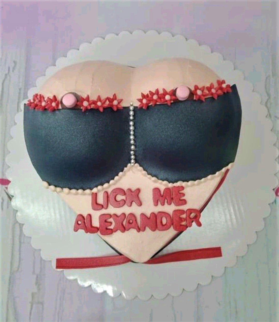 Heart-shaped novelty cake designed to look like a woman's torso wearing a black bra with red floral accents and a personalized message.