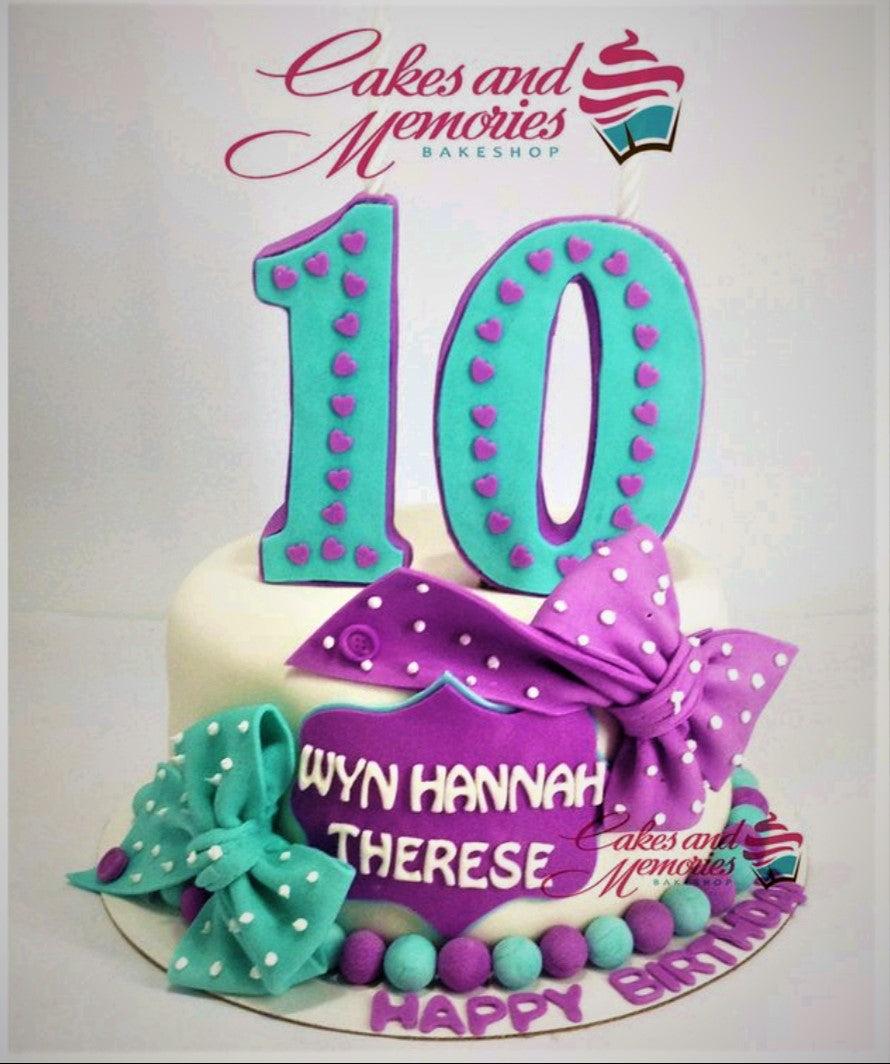 White fondant cake with large teal and purple number 10 toppers, teal and purple bows, and a purple name plaque.
