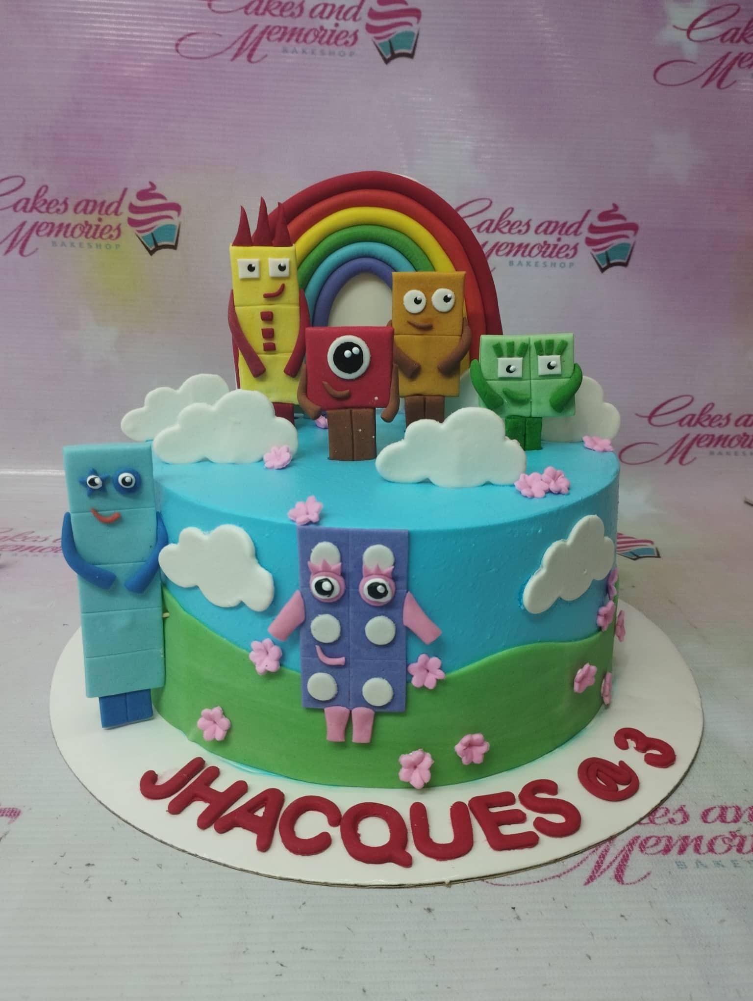 Numberblocks themed birthday cake with a blue and green landscape, rainbow, and fondant character figures.