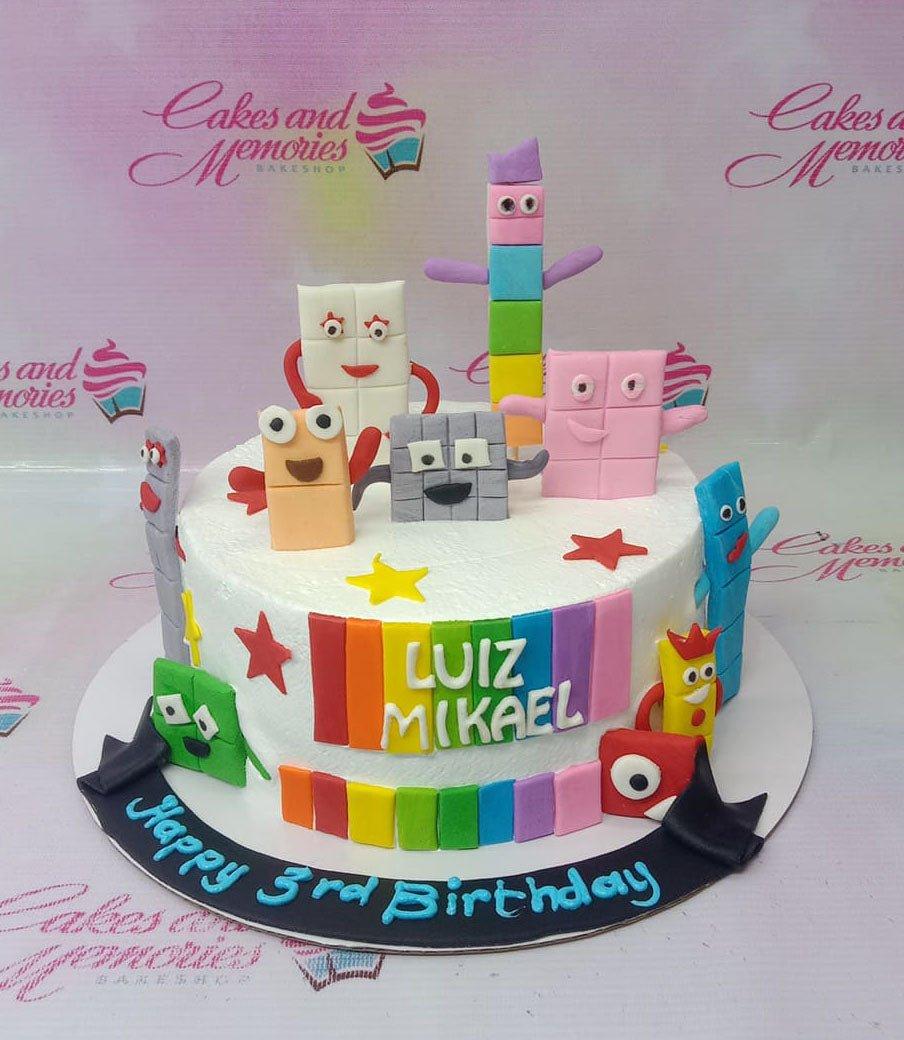 White round Numberblocks birthday cake with colorful fondant characters and a black banner message.