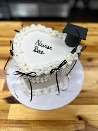 White heart-shaped vintage cake with white icing ruffles, black bows, gold pearls, and a black graduation cap topper.