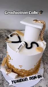 White graduation cake for a nurse featuring a 3D fondant graduation cap, stethoscope, syringe, and gold glitter accents.