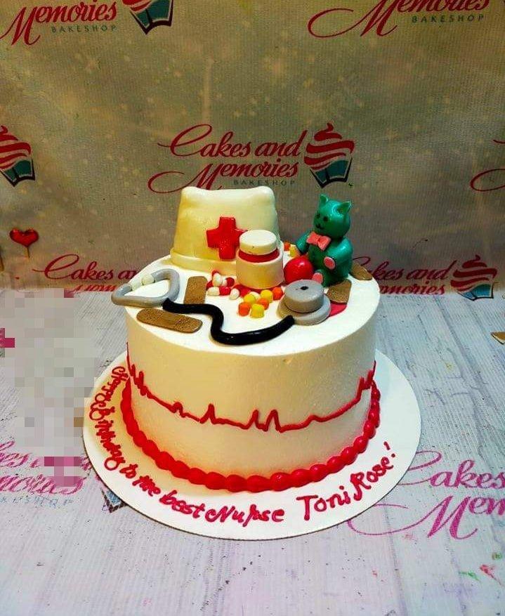 White nurse-themed birthday cake with fondant medical tools, a stethoscope, and a green teddy bear nurse figurine.