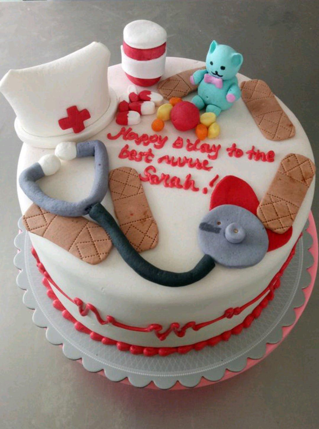 White fondant nurse-themed birthday cake with a stethoscope, nurse hat, bandages, and a blue bear figurine.