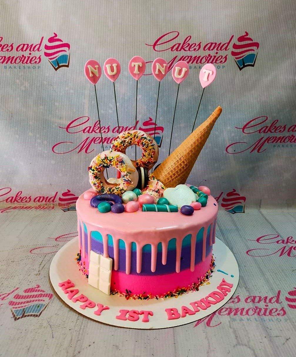 Pink and purple drip cake with donuts, ice cream cone, and balloon toppers for a 1st barkday celebration.