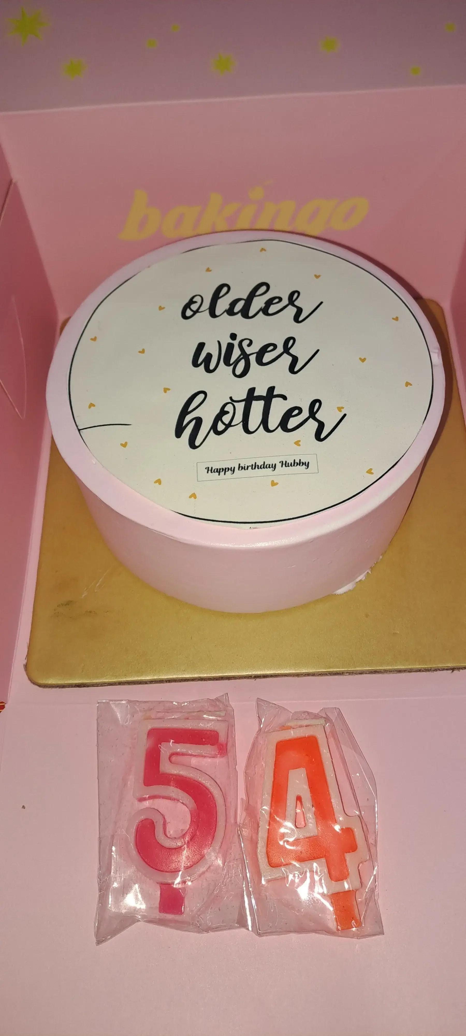 Pink bento cake with a white circular printout topper featuring the text Older Wiser Hotter and small gold hearts.