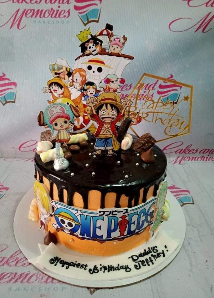 One Piece anime themed birthday cake with orange icing, chocolate drip, and various character printouts including Luffy and the Straw Hat crew.