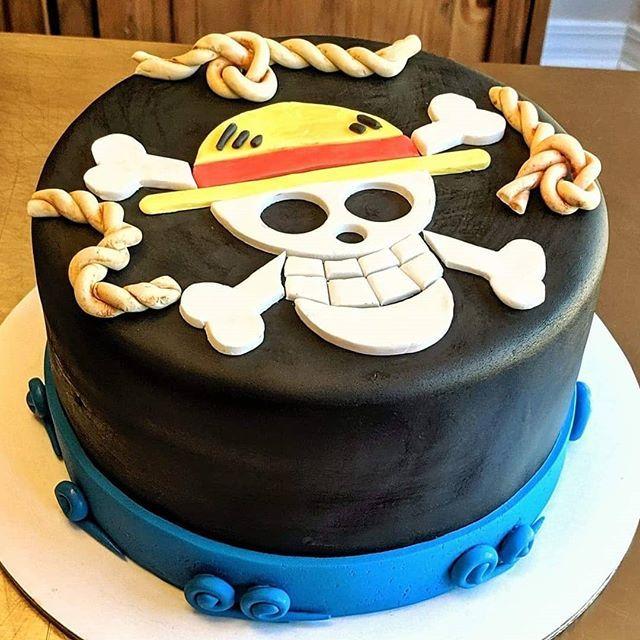 One Piece themed black fondant cake featuring the Straw Hat Pirates Jolly Roger skull and crossbones with a yellow straw hat and rope accents.