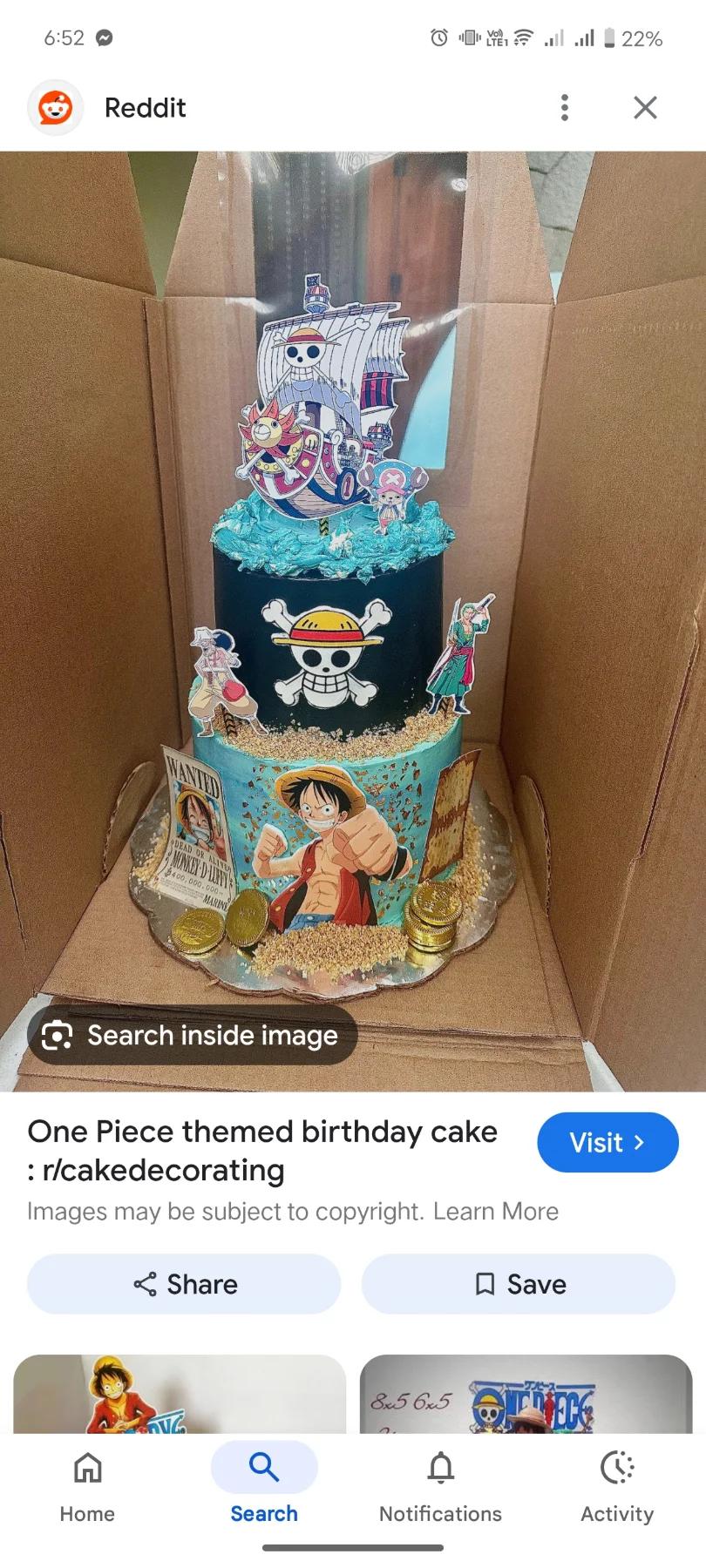 Two-tier One Piece anime themed birthday cake with black and blue icing, character printouts, and gold chocolate coins.