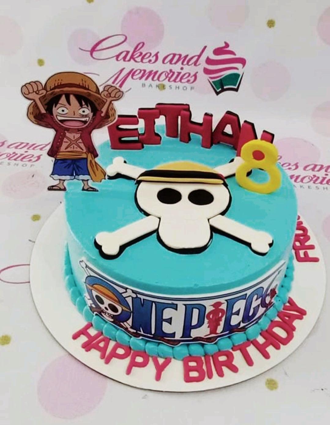 One Piece themed birthday cake with Luffy printout, gumpaste skull and crossbones, and pink lettering on a light blue icing base.