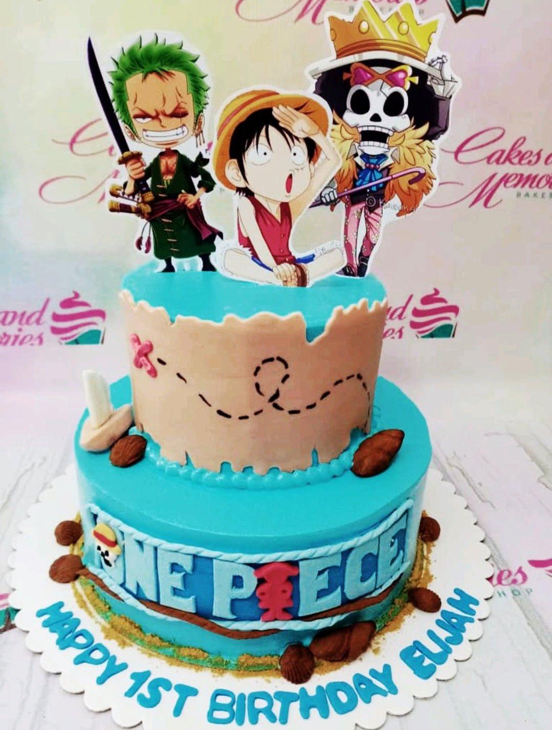 Two-tier One Piece themed birthday cake in light blue with character printouts, a treasure map panel, and edible shells.