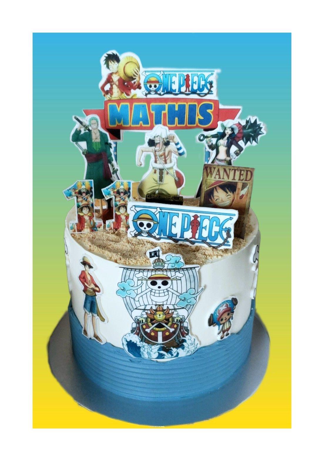 One Piece themed birthday cake with blue and white icing, sand-like crumbs, and various character printouts including Luffy and Zoro.