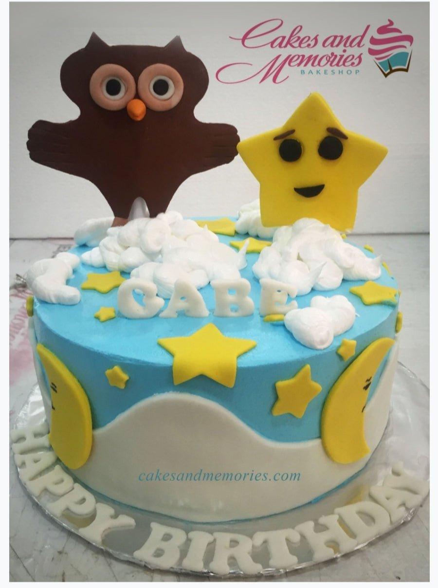 Blue and white sky themed birthday cake with a brown owl and yellow star fondant toppers, featuring clouds and crescent moons.