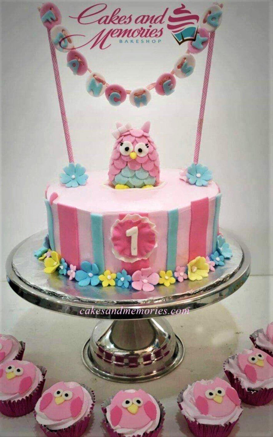 Pink and blue striped owl birthday cake with a pink fondant owl topper and colorful gumpaste flowers.