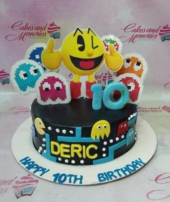 Black Pac-Man themed birthday cake with colorful ghost printouts, a large yellow Pac-Man topper, and blue number 10.
