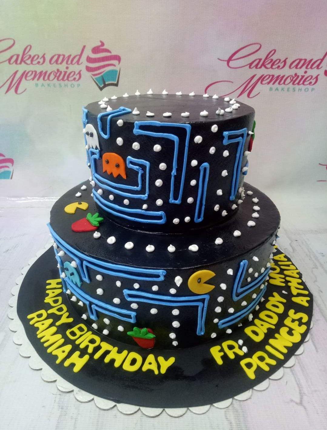 Two-tier black Pac-Man themed birthday cake with blue icing maze lines, colorful ghosts, and yellow Pac-Man figures.