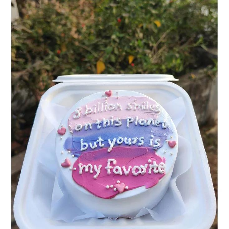 White bento cake with pink, purple, and blue palette knife icing strokes, white piped message, and pink heart decorations.