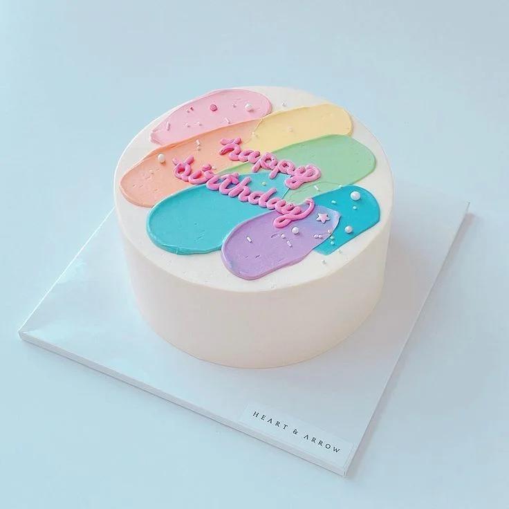 Minimalist white cake with colorful palette knife icing strokes in pink, yellow, green, blue, and purple with a pink Happy Birthday message.
