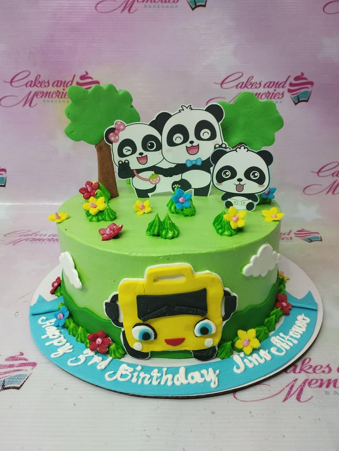 Green panda and bus themed birthday cake with 3D panda toppers and a yellow bus decoration on the side.