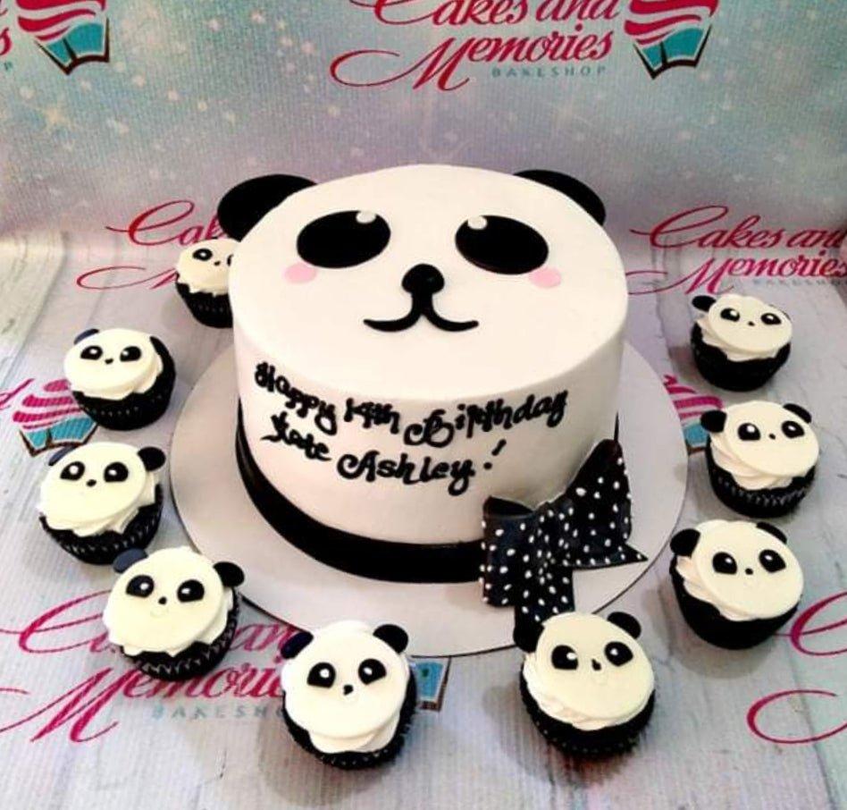 White panda-themed birthday cake with black fondant ears and face, featuring a black and white polka dot bow and matching panda cupcakes.