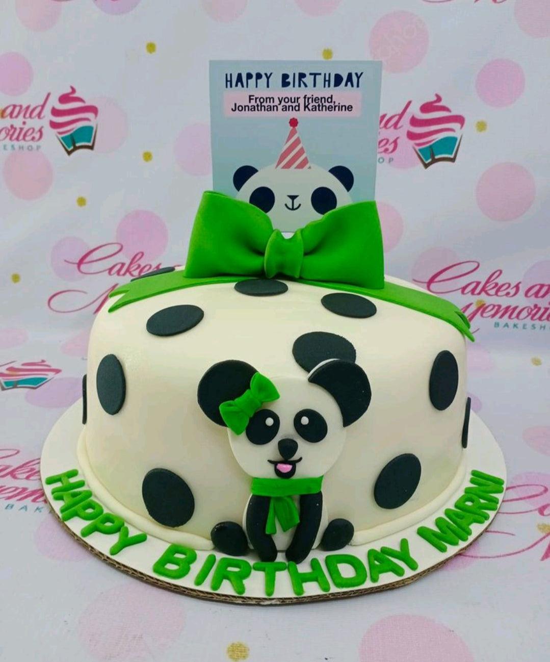 White fondant panda cake with black polka dots and a large green bow on top.