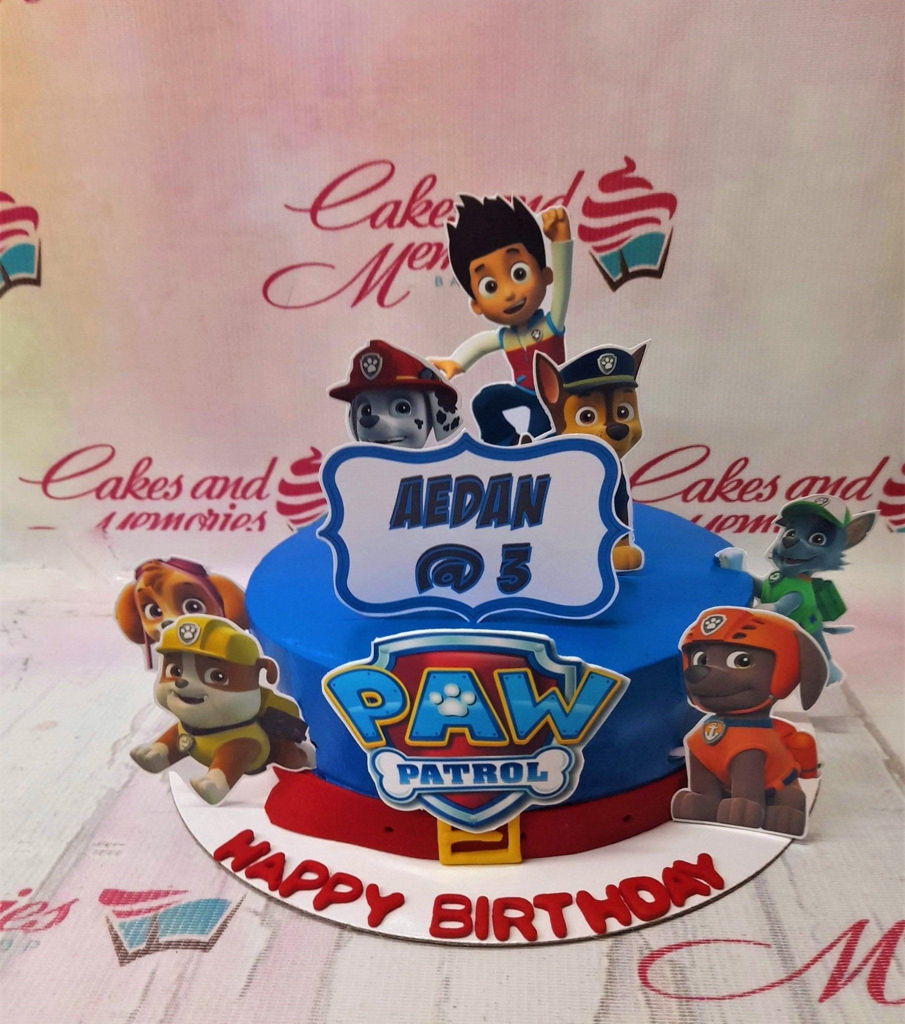 Blue Paw Patrol themed birthday cake with character printouts and a red fondant belt detail.