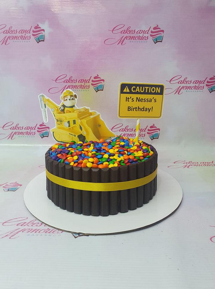 Paw Patrol themed chocolate cake with KitKat border, colorful M&M topping, and a construction pup topper.