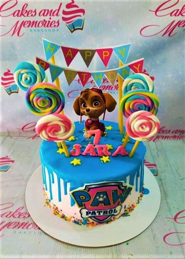 Blue Paw Patrol Skye themed cake with colorful lollipops, stars, and a pink drip effect.