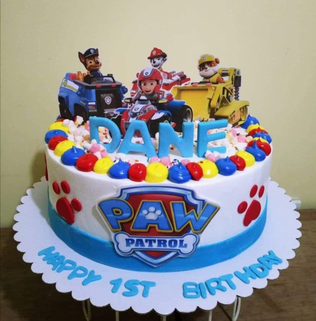 Paw Patrol themed birthday cake with blue and white icing, character printouts, and colorful icing dollops.