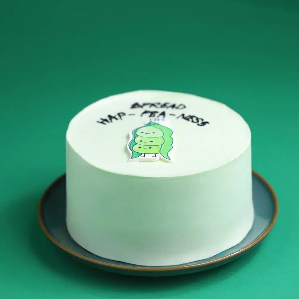 Light green bento cake with a cute pea pod printout and the message Spread Hap-pea-ness in black icing.