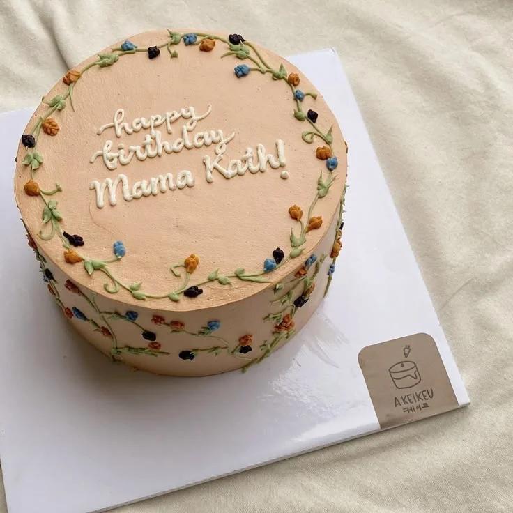 Peach minimalist birthday cake with delicate piped floral vines and white icing message for Mama Kath.