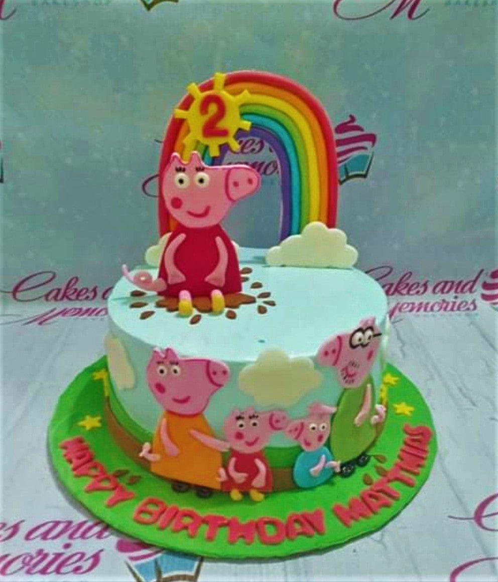 Peppa Pig themed light blue fondant cake with a rainbow, sun, and fondant family figures on a green base board.