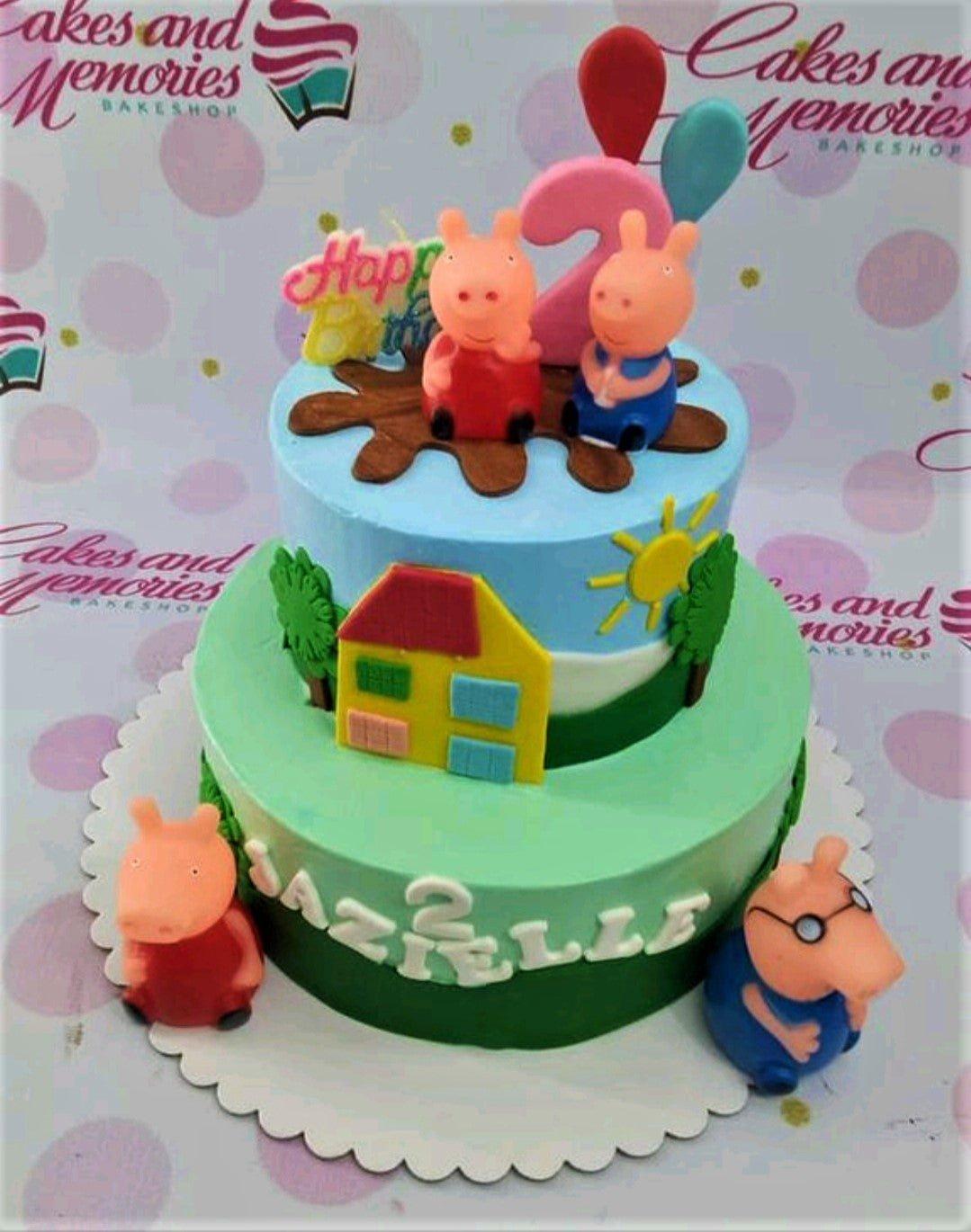 Two-tier Peppa Pig themed birthday cake with fondant figures of Peppa, George, Mummy, and Daddy Pig on a green and blue landscape.
