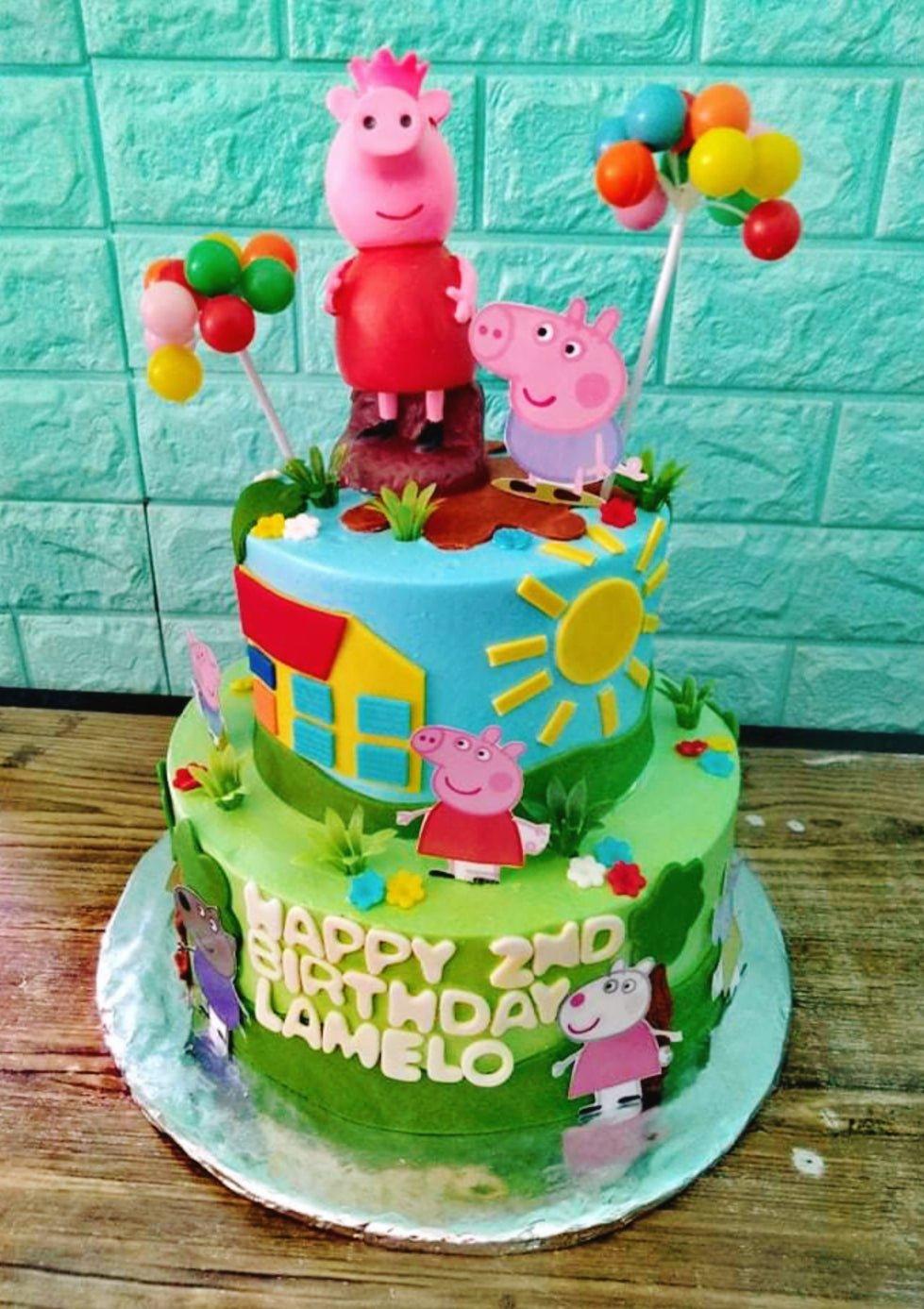 Two-tier Peppa Pig themed birthday cake with blue and green fondant, character printouts, and a 3D Peppa Pig figure on top.