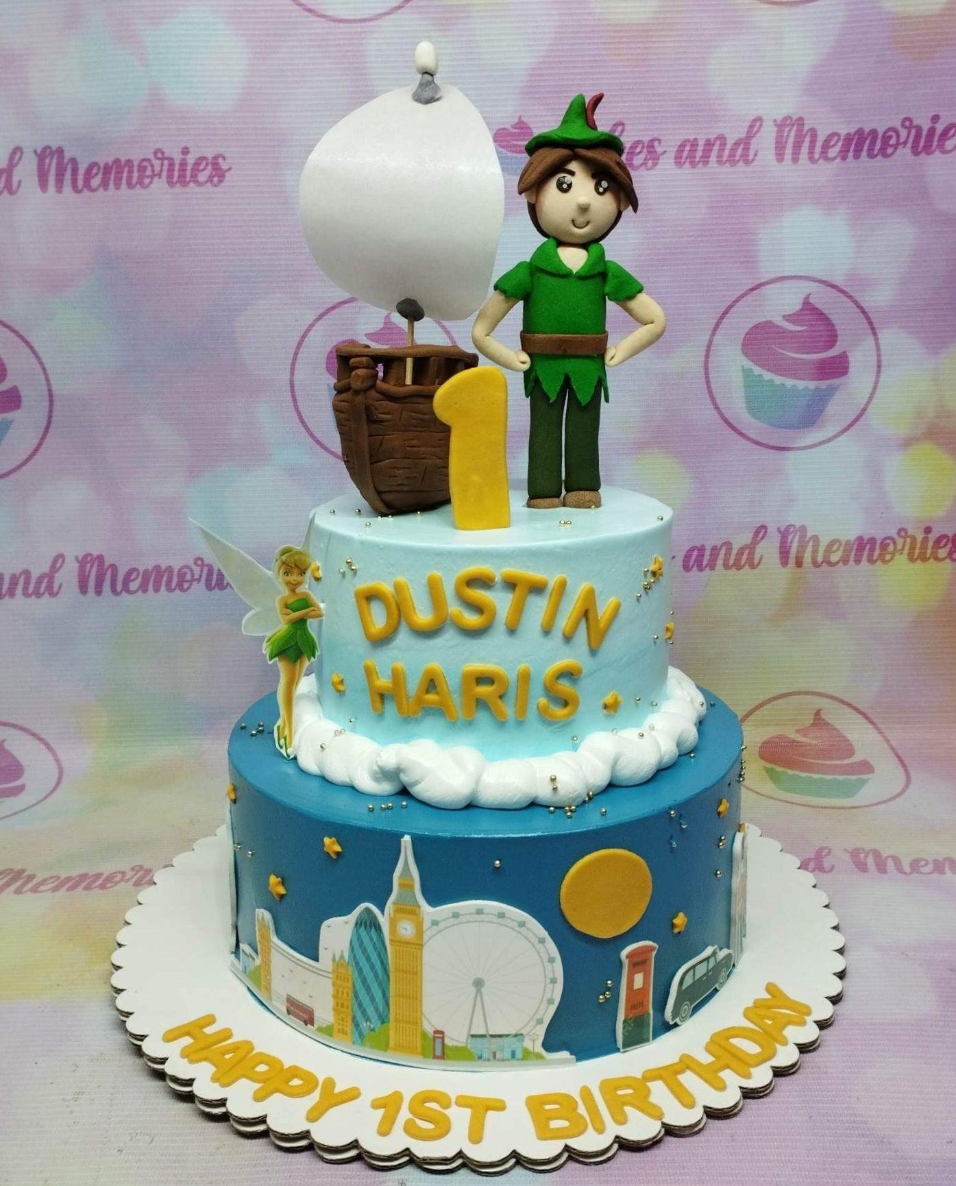 Two-tier Peter Pan themed birthday cake in light and dark blue with fondant figures of Peter Pan, a pirate ship, and Tinkerbell.