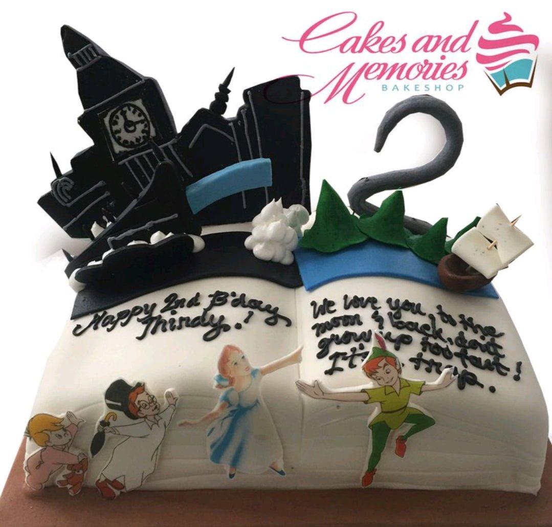 Peter Pan themed open book cake with fondant figures of Peter Pan, Wendy, and the Darling children, featuring a Big Ben silhouette and Neverland scenery.