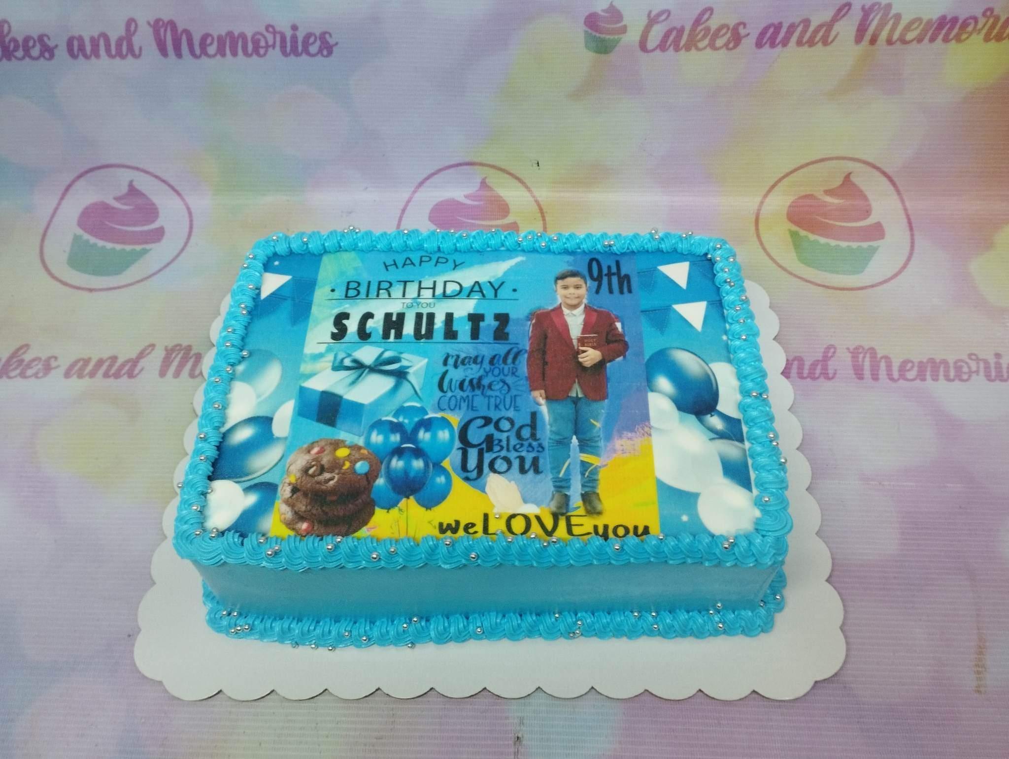 Light blue rectangular birthday cake with a large edible photo print of a boy, blue balloons, and silver dragees on piped icing borders.