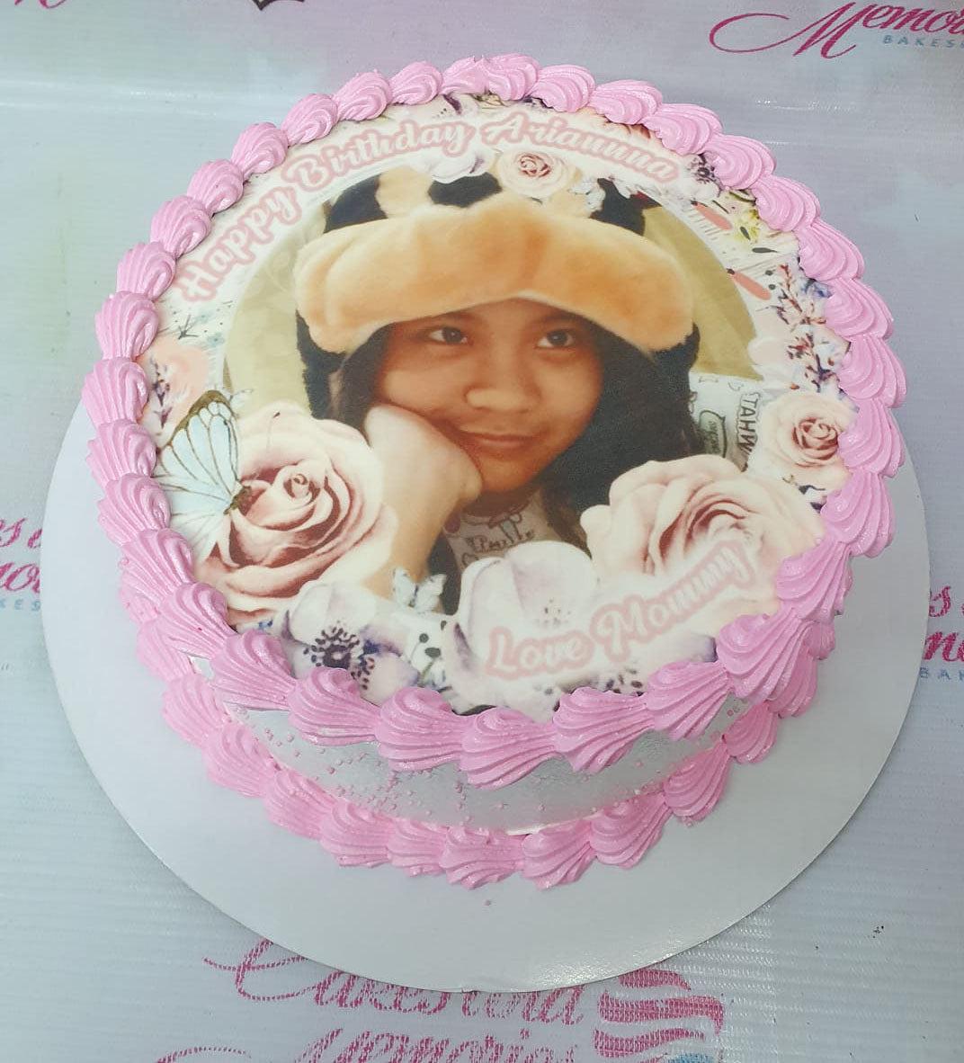 White round cake with pink icing borders and a large edible photo print of a girl surrounded by roses and butterflies.