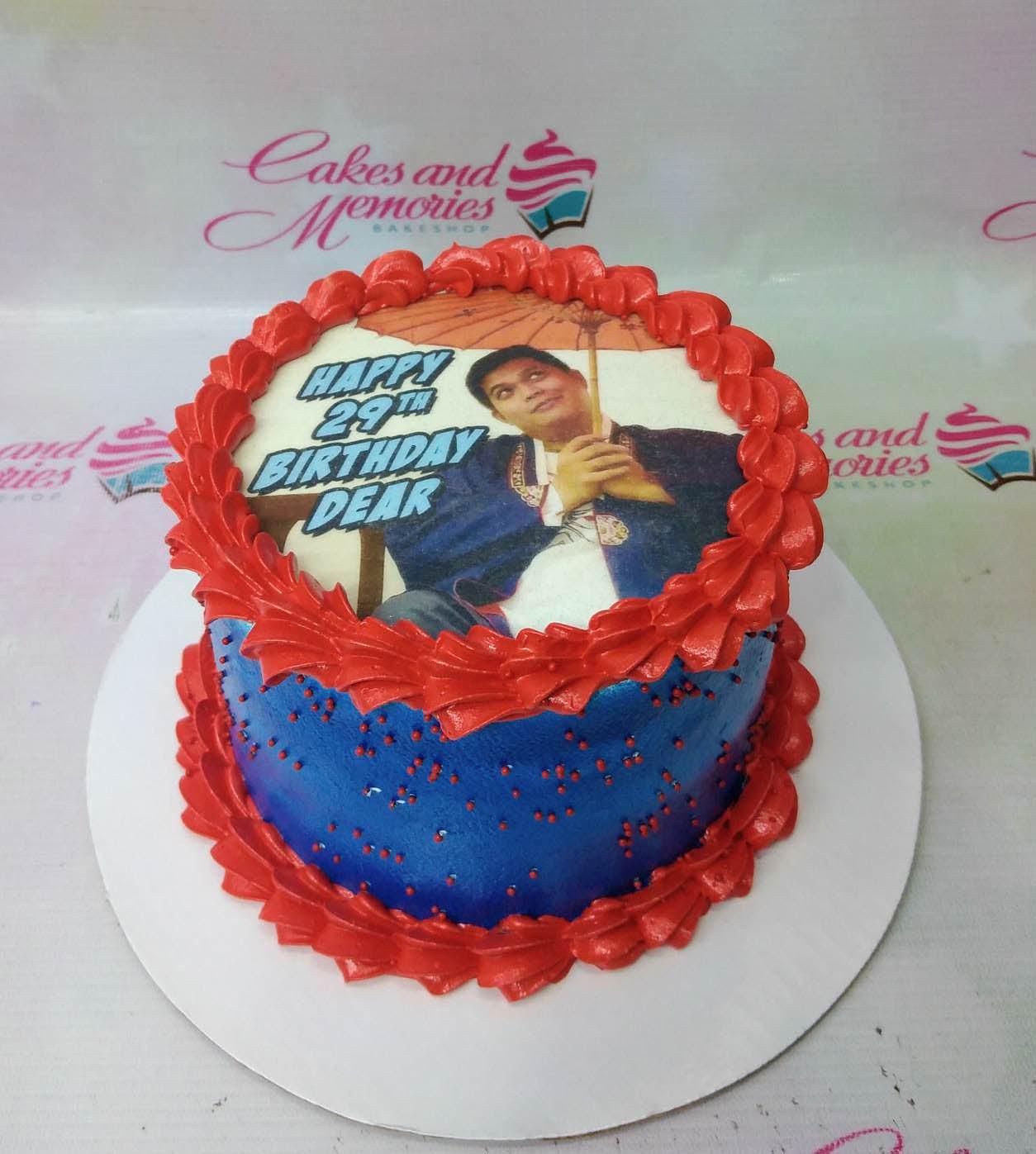 Blue and red birthday cake with a large photo printout of a man under an umbrella and red icing borders.