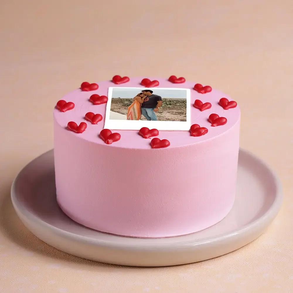 Pink minimalist cake with a polaroid-style photo print and red icing hearts on top.