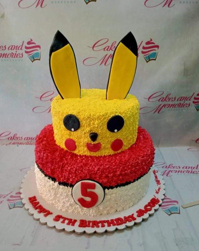 Two-tier Pikachu and Pokeball themed birthday cake with yellow and red textured icing and fondant ears.