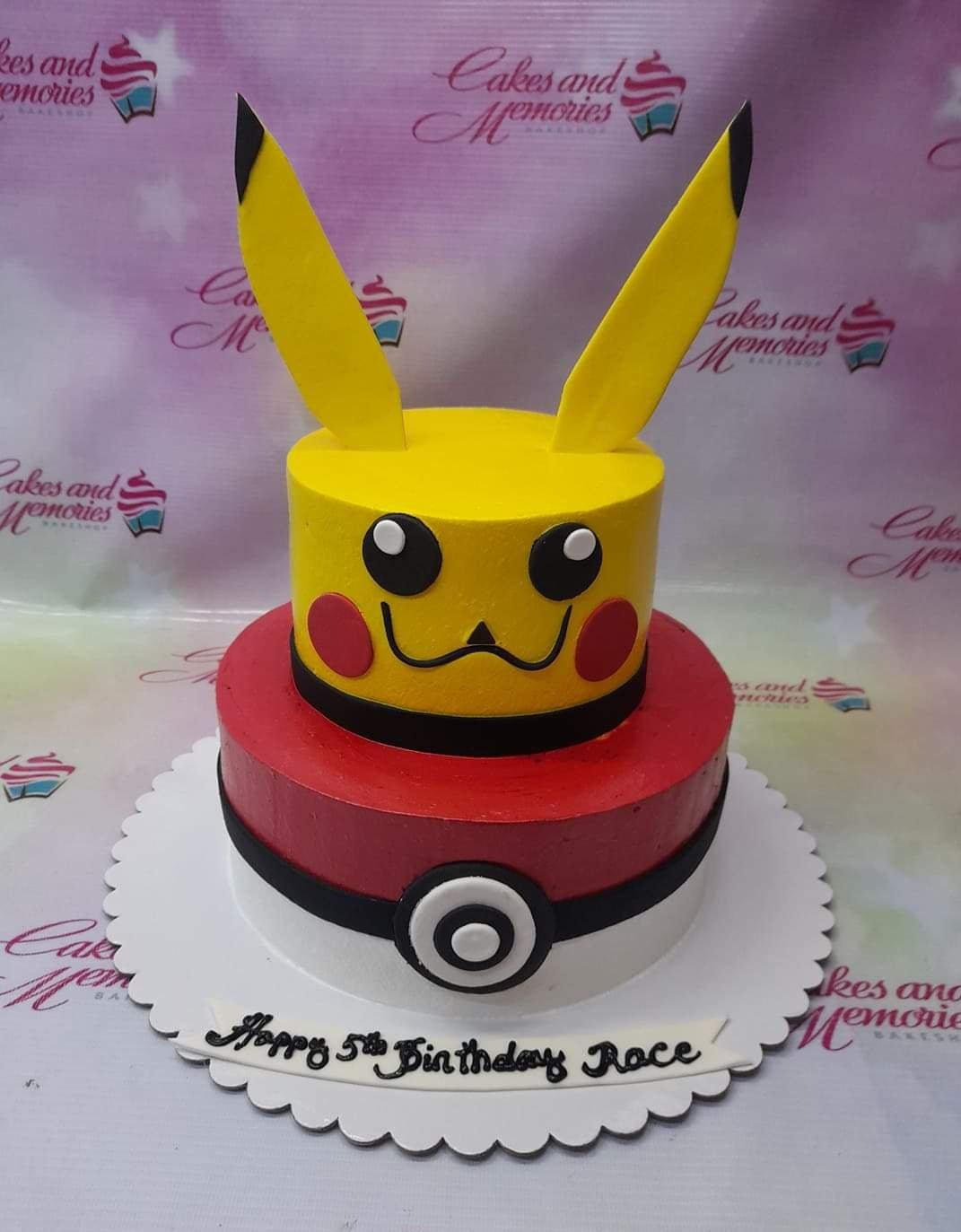 Two-tier Pikachu and Pokeball themed birthday cake with yellow and red icing and a Happy Birthday message.