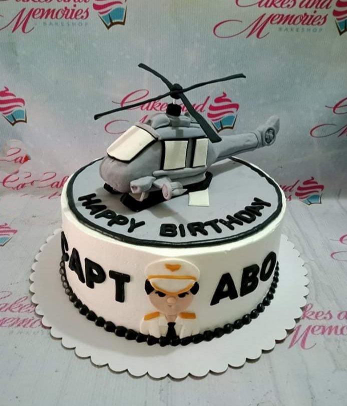 White 1-tier pilot themed birthday cake with a large grey fondant helicopter topper and a fondant pilot figure on the side.