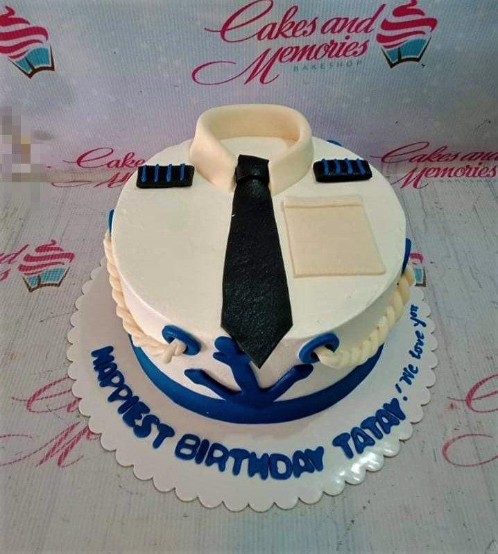 White pilot uniform themed cake with a black tie, blue anchor, and epaulettes for a birthday celebration.