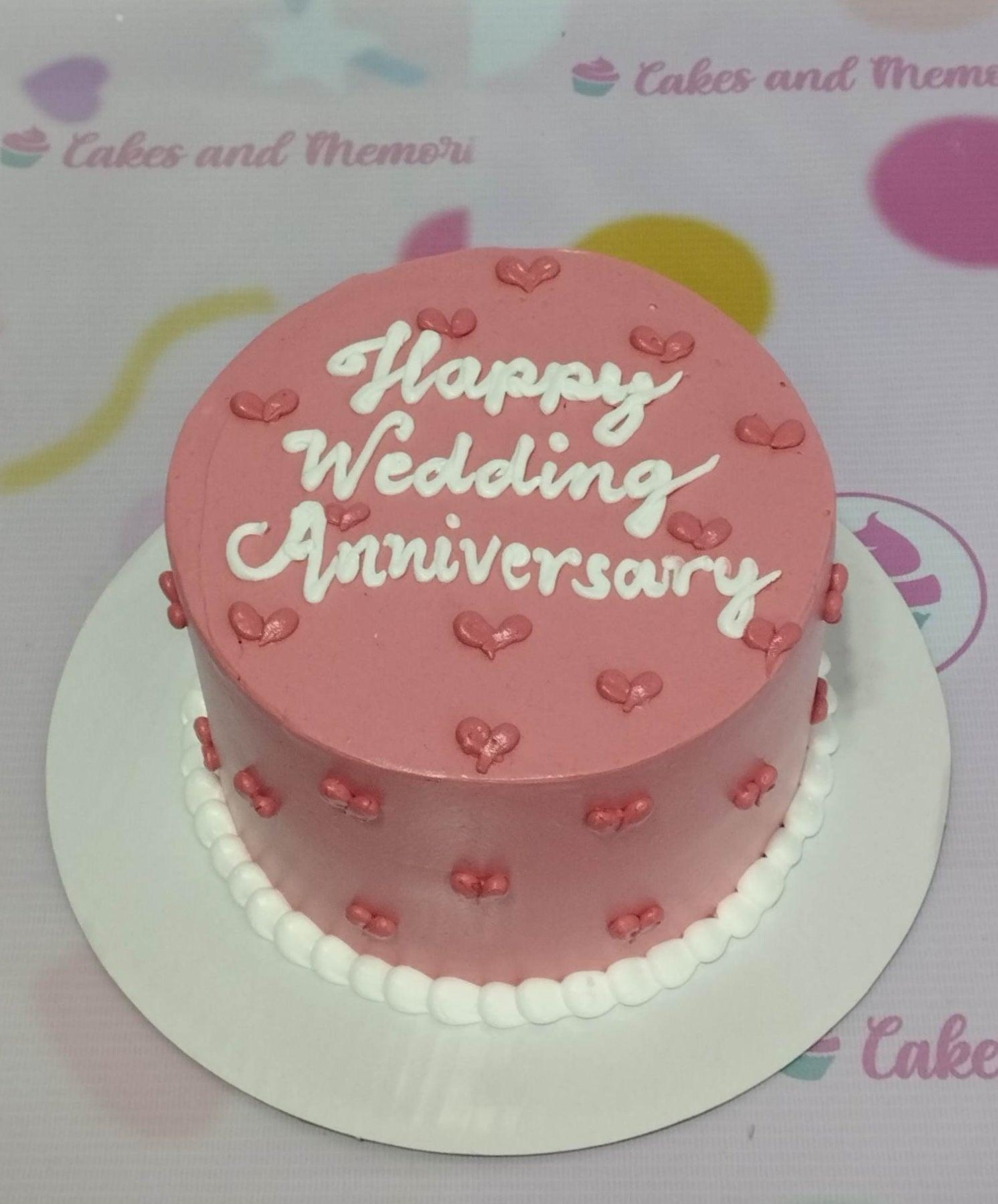 Pink minimalist wedding anniversary cake with white icing text and small pink heart decorations.