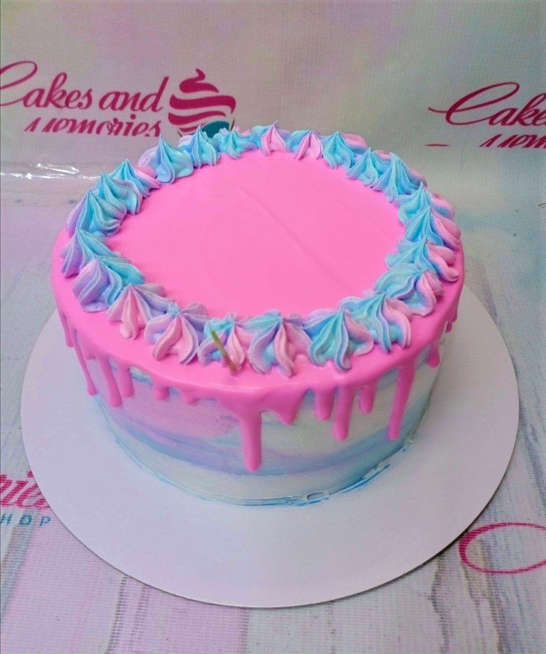 Single tier pink and blue watercolor cake with pink drip and two-tone icing rosettes on top.