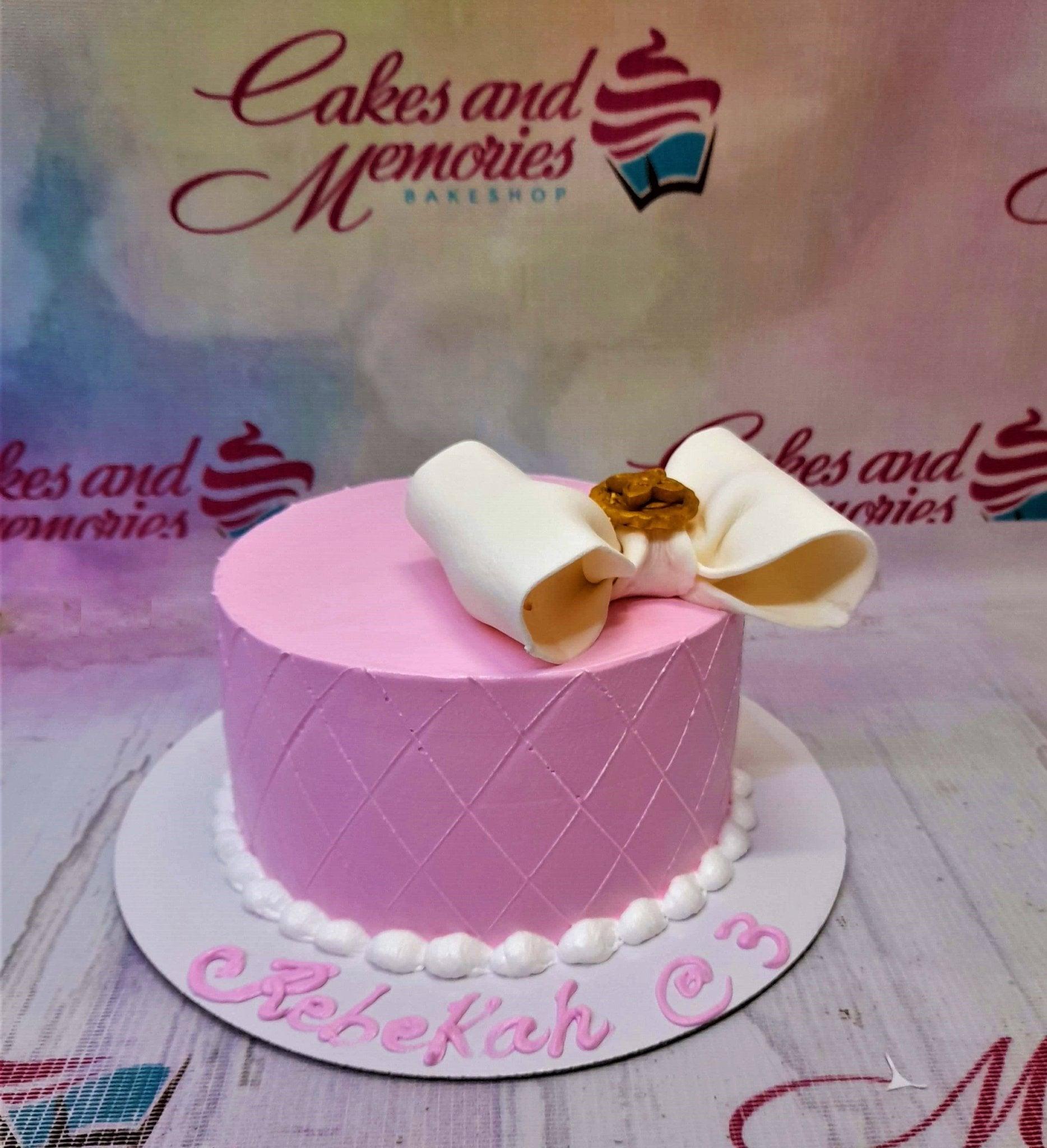Pink minimalist cake with a large white fondant bow and quilted pattern on the side, featuring a pink message on the base board.